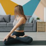 Beautiful young woman is doing yoga relaxing in lotus asana with hands in namaste gesture meditating at home. Relaxation, modern lifestyle and apartment concept.