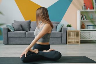 Beautiful young woman is doing yoga relaxing in lotus asana with hands in namaste gesture meditating at home. Relaxation, modern lifestyle and apartment concept.