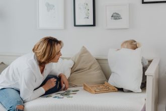 A mother interacting with her daughter hiding behind a pillow, enjoying quality time indoors.