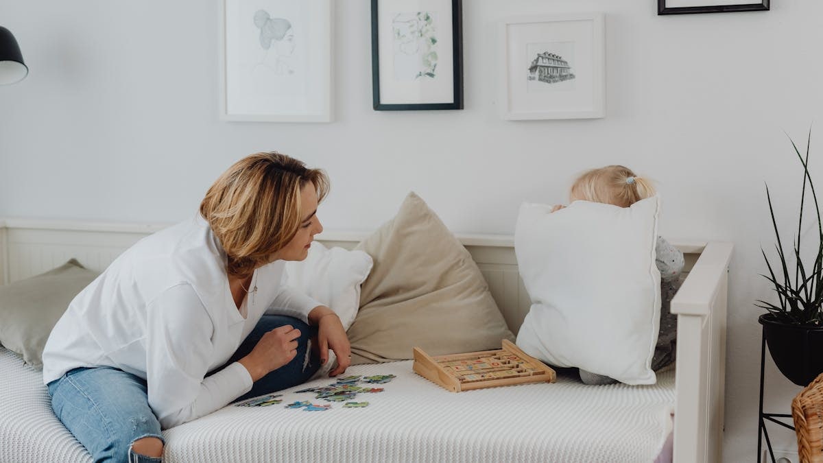 A mother interacting with her daughter hiding behind a pillow, enjoying quality time indoors.